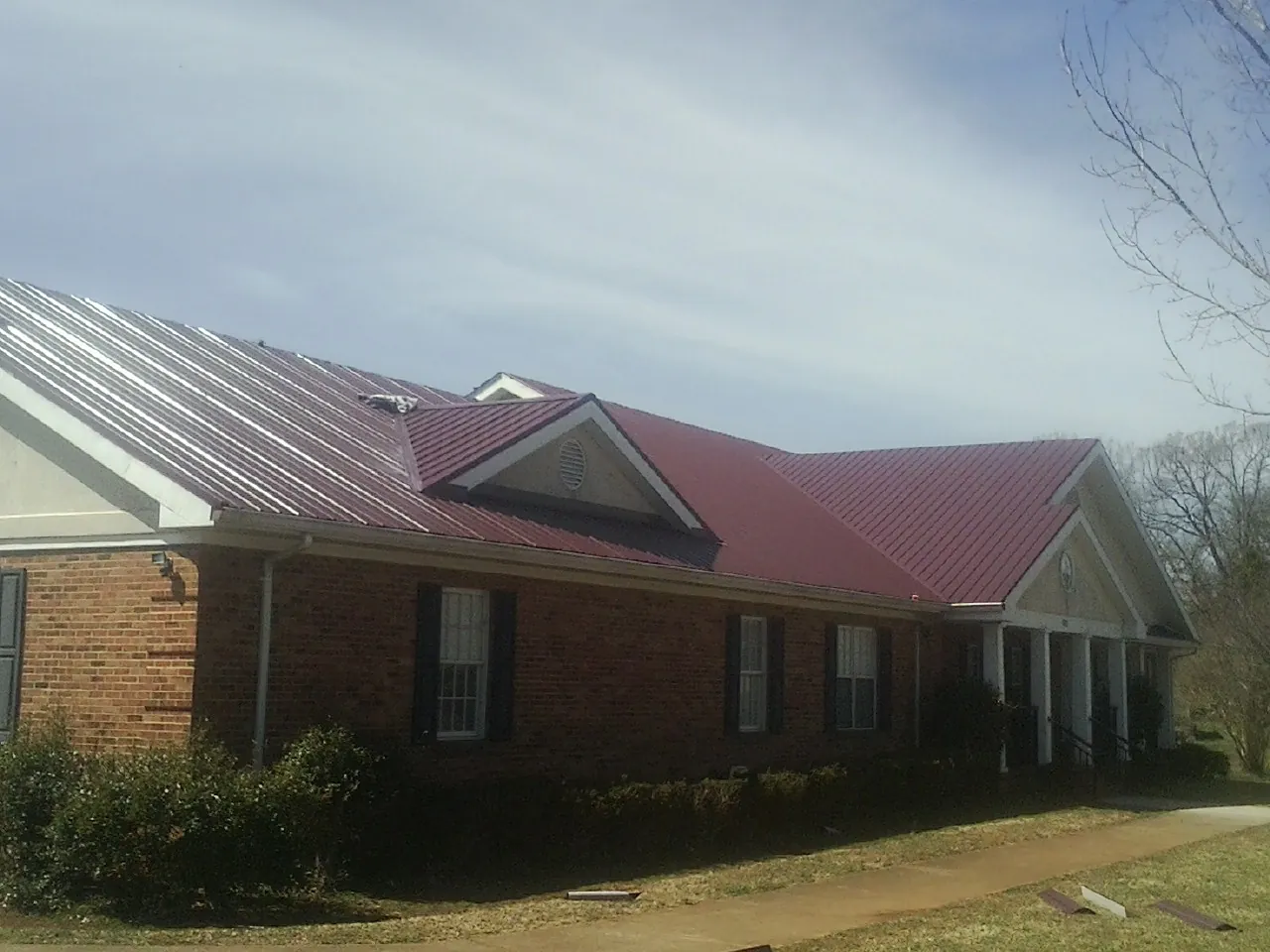 Red metal roof with gabled entries on a long brick building, from a Hail Damage Roof Repair job in Geneseo