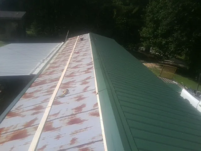Old rusted panels beside newly installed green metal roofing — Wind Damage Roof Repair by Roofing Brothers in Geneseo