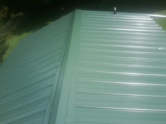 New green metal panels meeting at the ridge of a roof — Flat Roof Repair work by our crew in Geneseo