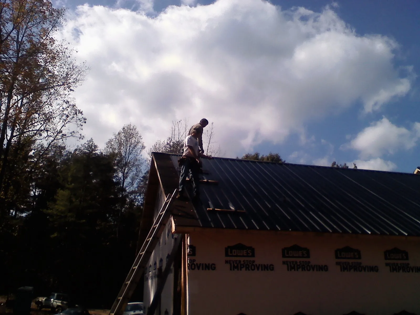 Roofer fastening dark metal panels high against a cloudy sky, from a Roof Inspection job in Geneseo
