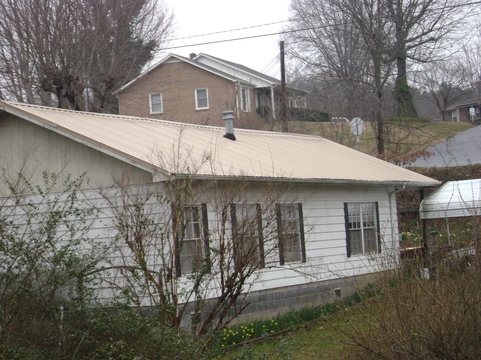 Tan metal roof on a white sided house set into a hillside — Commercial Roofing by Roofing Brothers in Geneseo