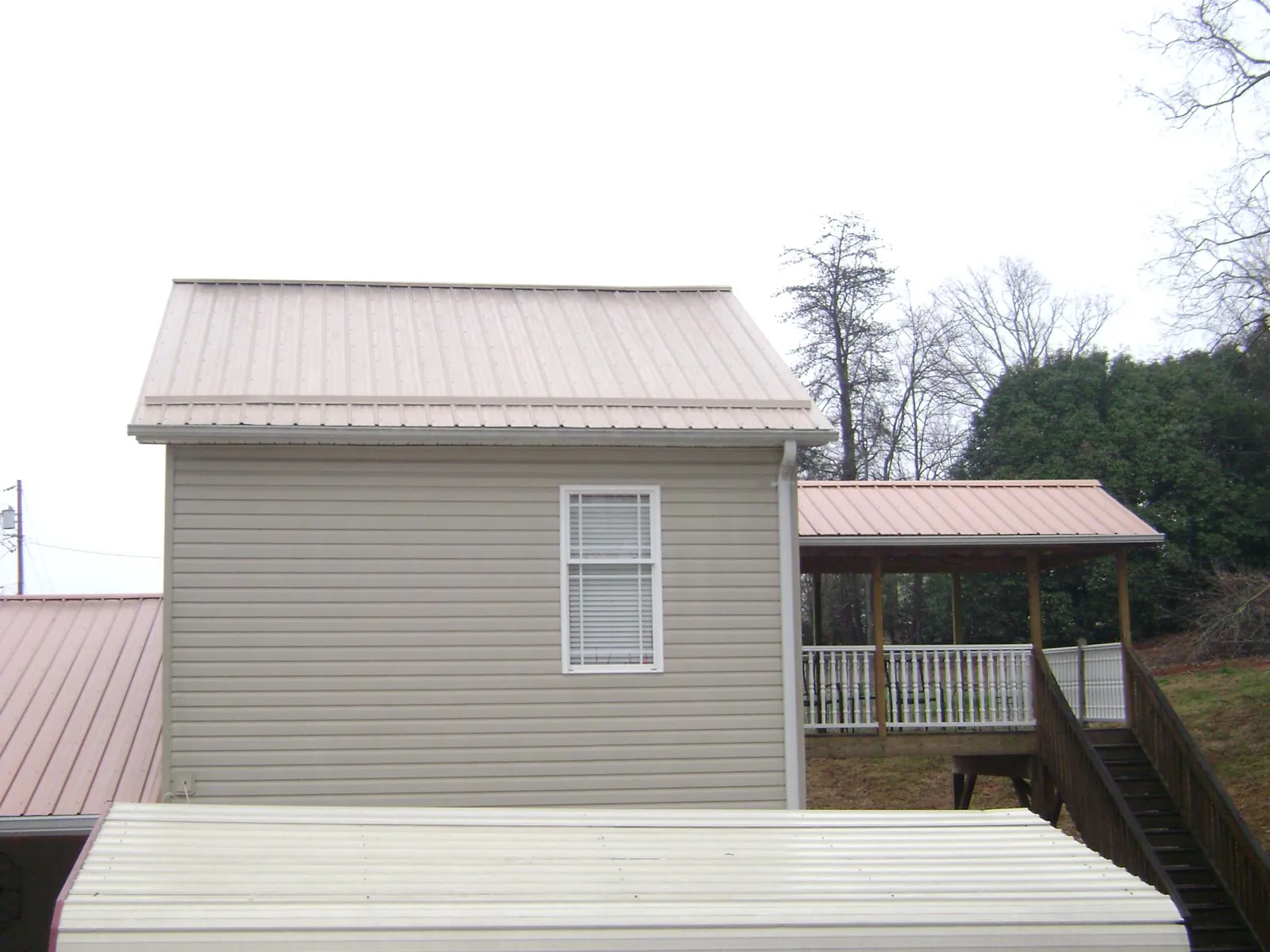 Tan metal roofs on a two story addition and attached porch, from a Roof Replacement job in Geneseo